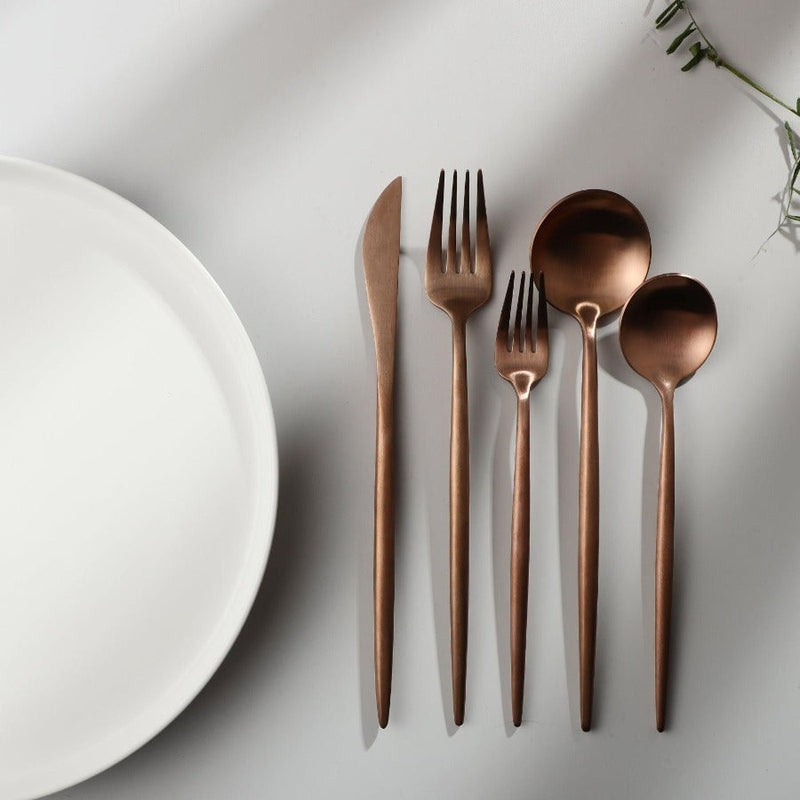 Kupferbesteck-Set auf weißem Tisch, minimalistisches Design, Gabel, Messer, Löffel, Teller.