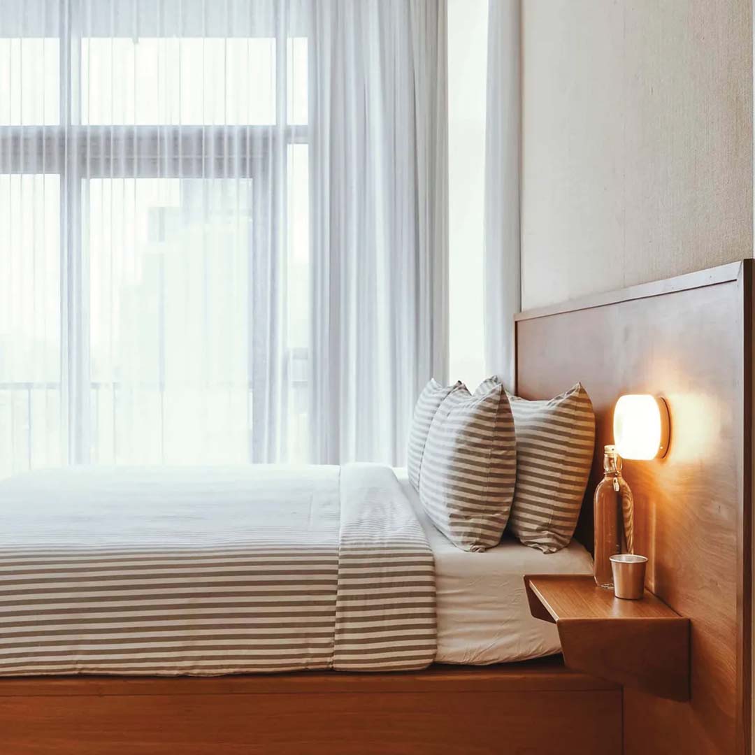 Modernes Schlafzimmer mit Holzbett, gestreifter Bettwäsche, Nachttischlampe, minimalistisches Design.