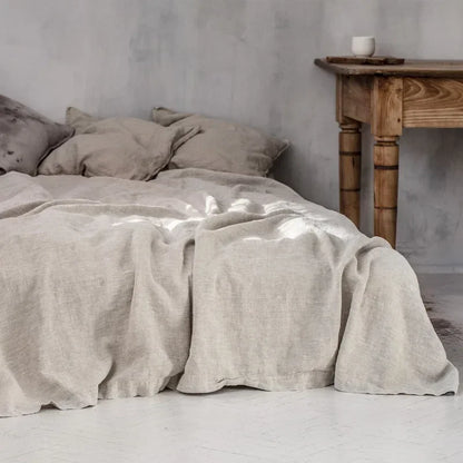 Beiges Leinenbettwäsche-Set auf Bett, rustikaler Holztisch, skandinavisches Schlafzimmer-Design.