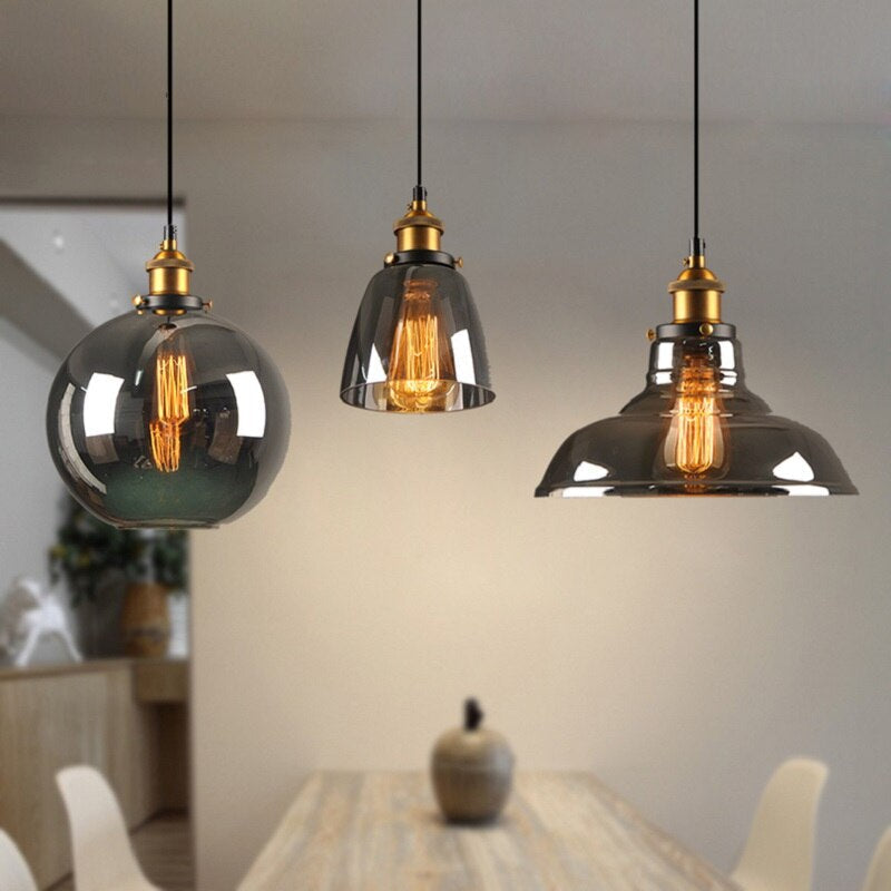 Drei moderne Pendelleuchten aus Glas mit Edison-Glühbirnen über einem Holztisch.