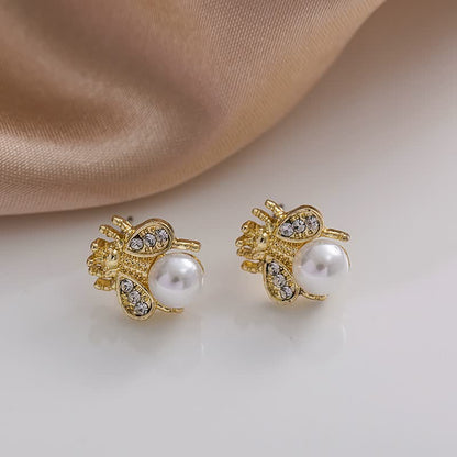 Goldene Bienen-Ohrringe mit Perlen und Strasssteinen auf weißem Hintergrund, eleganter Schmuck.