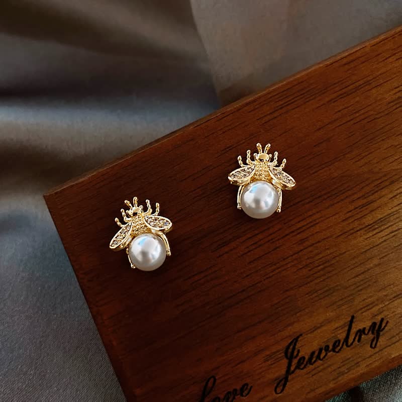 Goldene Bienen-Ohrringe mit Perlen, eleganter Schmuck auf Holzuntergrund.