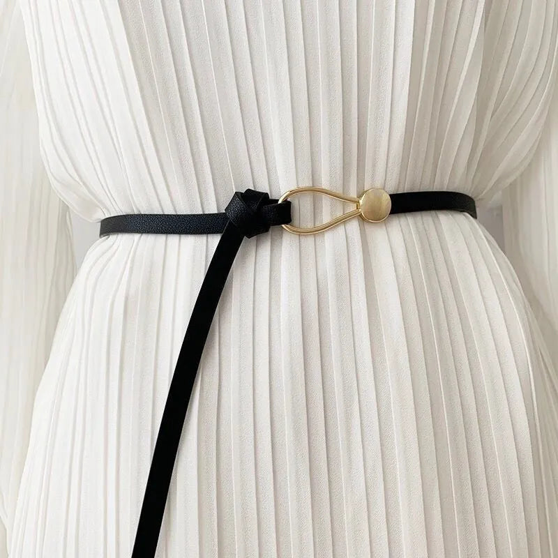 Schwarzer Ledergürtel mit goldener Schnalle auf weißem Plisseekleid.