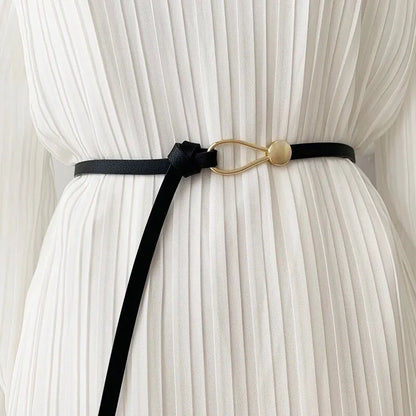 Schwarzer Ledergürtel mit goldener Schnalle auf weißem Plisseekleid.