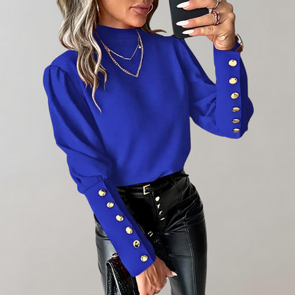 Frau in blauem Pullover mit goldenen Knöpfen, schwarze Lederhose, Smartphone in der Hand.