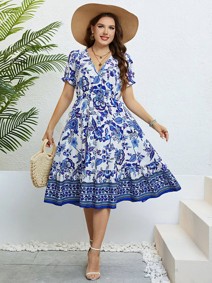 Frau im blauen Blumen-Sommerkleid mit Strohhut und Korbtasche vor weißer Wand.