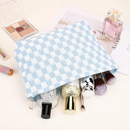 Hellblau-weiß karierte Kosmetiktasche mit Make-up-Pinseln und Parfümflasche auf hellem Hintergrund.