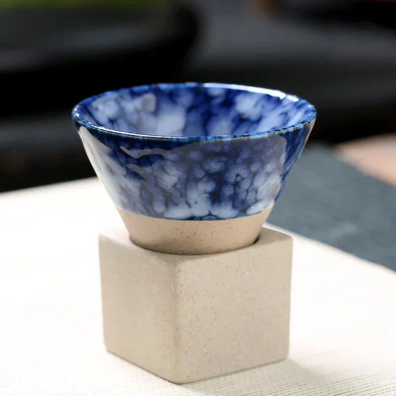 Blauer Keramikbecher mit Marmor-Effekt auf beigem Sockel, stilvolles Geschirr, modern.