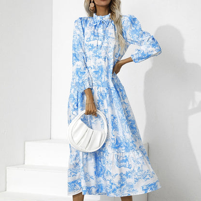 Frau in blau-weißem Maxikleid mit Blumenmuster, hält weiße Handtasche, Modefotografie.