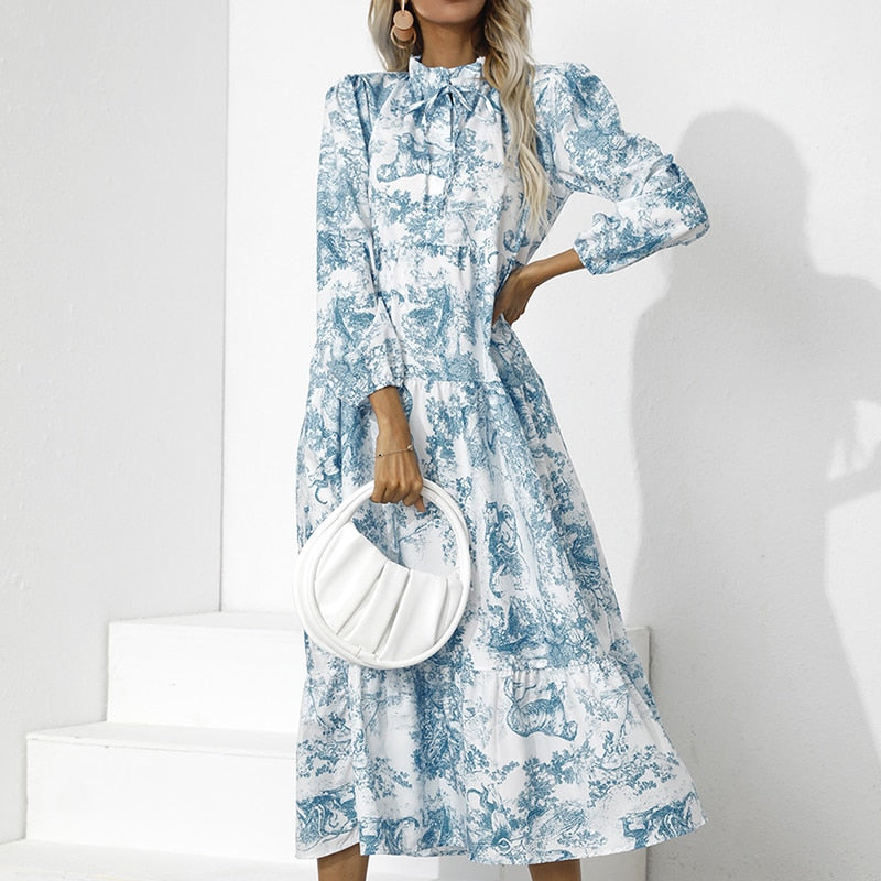 Frau in blau-weißem Maxikleid mit Muster, hält weiße Handtasche, elegante Mode.