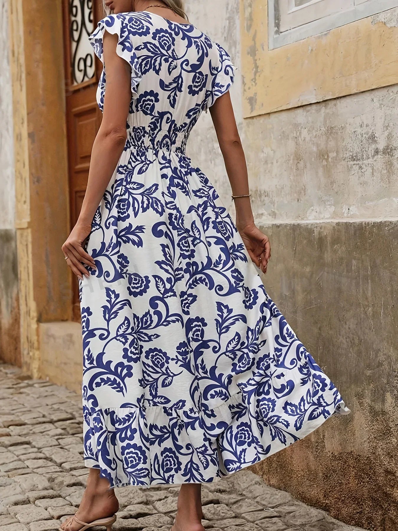 Frau in weißem, blau gemustertem Sommerkleid auf Kopfsteinpflasterstraße.