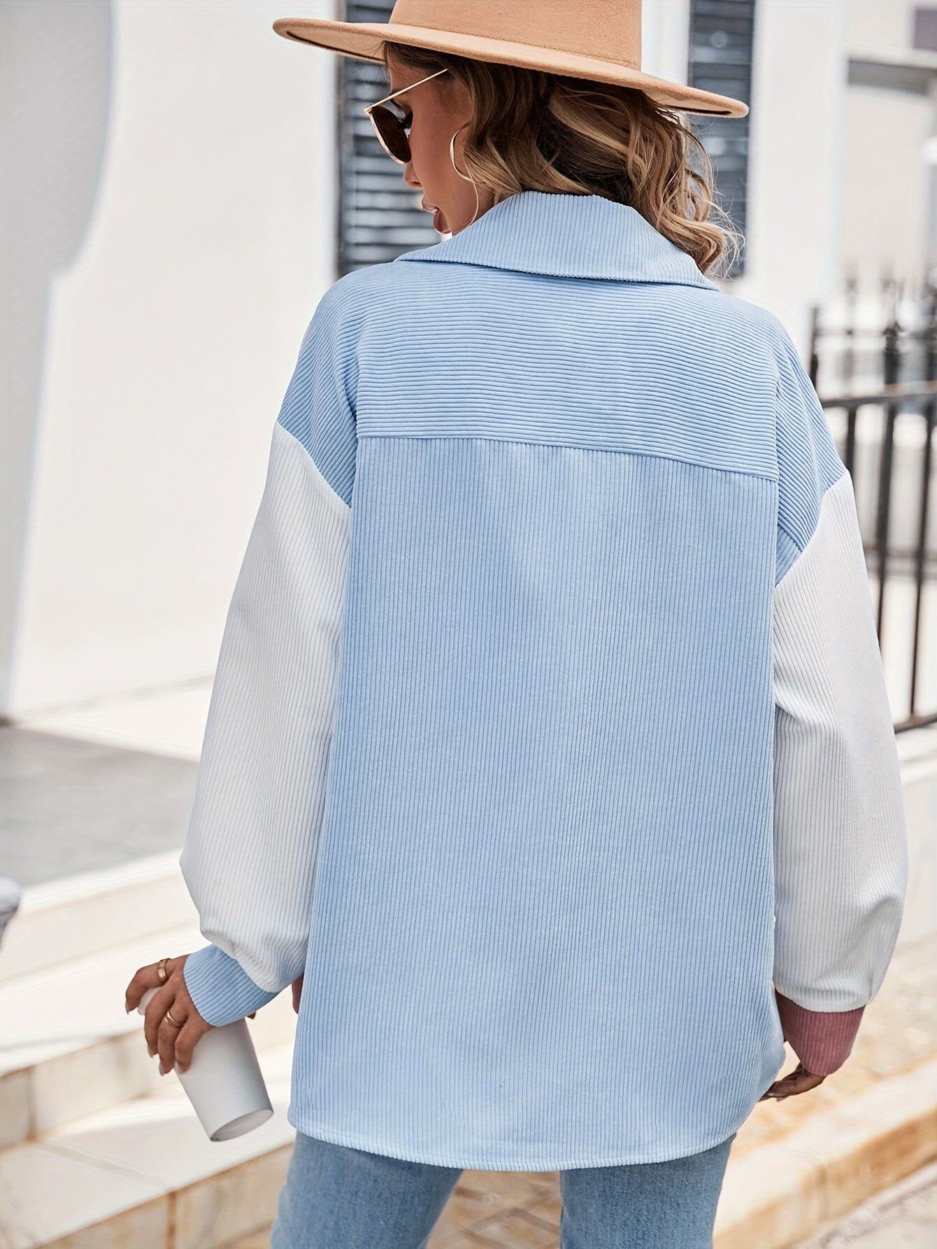 Frau in hellblauer gestreifter Bluse und Hut, hält weiße Flasche, modischer Streetstyle.