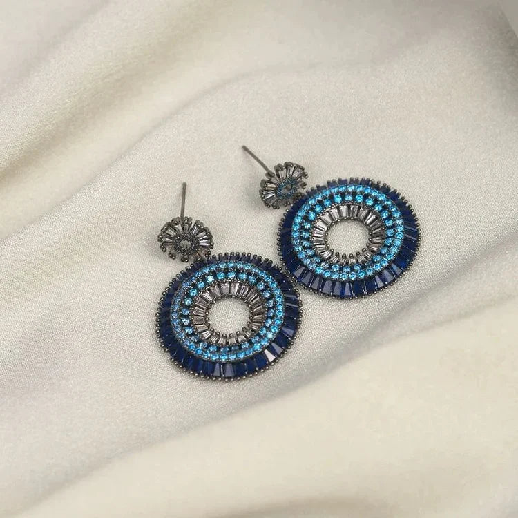 Blaue runde Ohrringe mit Kristallen auf weißem Stoff, eleganter Schmuck, Damenaccessoire.