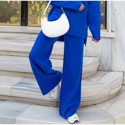 Frau in blauem Anzug mit weißer Tasche und Sneakers auf Marmortreppe.