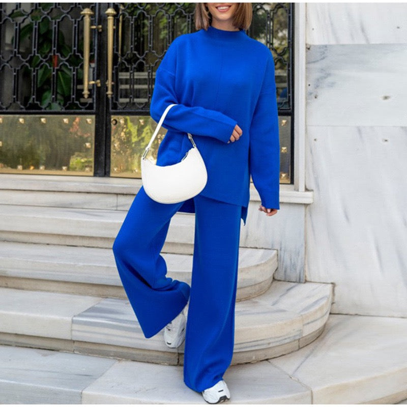 Frau in blauem Zweiteiler mit weißer Handtasche auf Marmortreppe, modisch, elegant.