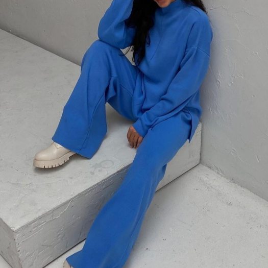 Frau in blauem Oversize-Sweatshirt und Hose, beige Stiefel, minimalistischer Hintergrund.