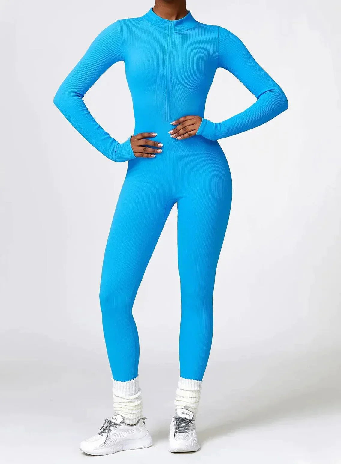 Frau in blauem, nahtlosem Sportanzug, Langarm, Ganzkörper, Fitnessmode, vor grauem Hintergrund.