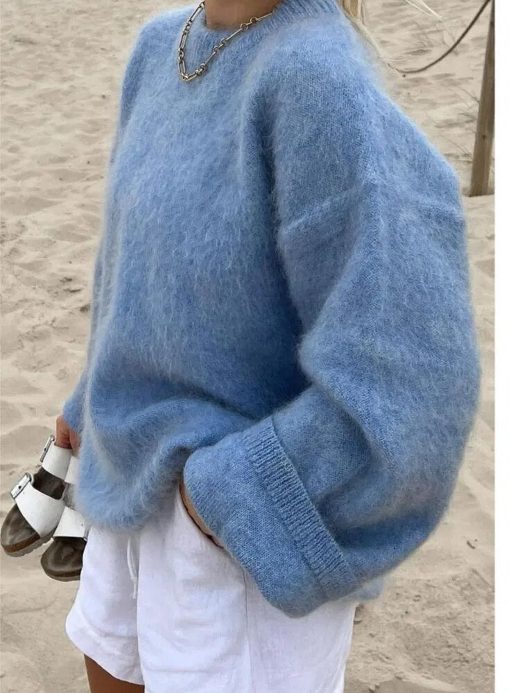 Frau in blauem, oversized Strickpullover am Strand, kombiniert mit weißen Shorts.
