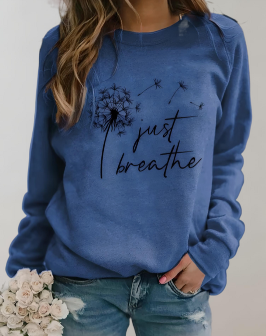 Frau in blauem Pullover mit "Just Breathe"-Aufdruck, hält weiße Rosen, lässige Mode.