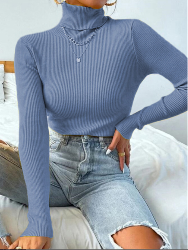 Frau in blauem Rollkragenpullover und zerrissenen Jeans auf Bett sitzend, modisch, lässig.