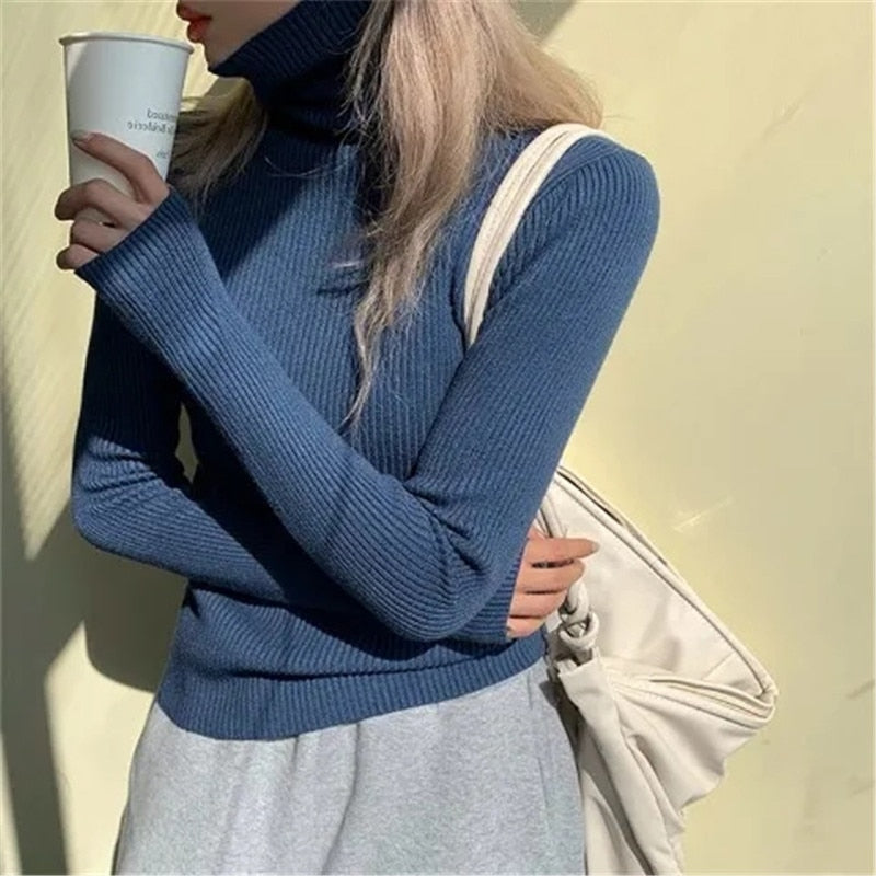 Frau in blauem Rollkragenpullover mit Kaffeebecher und weißer Tasche vor gelbem Hintergrund.