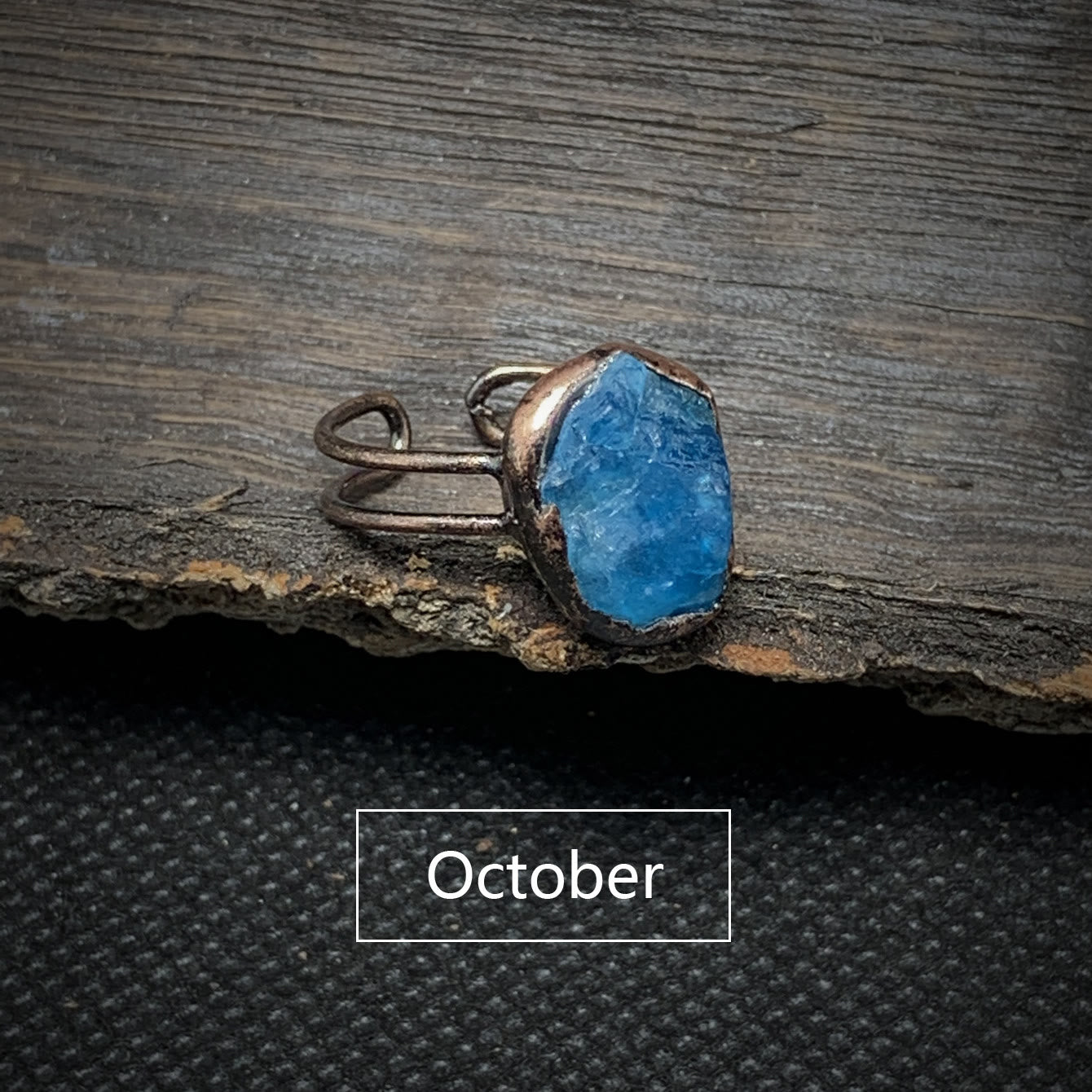 Rauher blauer Edelsteinring aus Kupfer auf Holzoberfläche, handgefertigter Schmuck, Oktober.