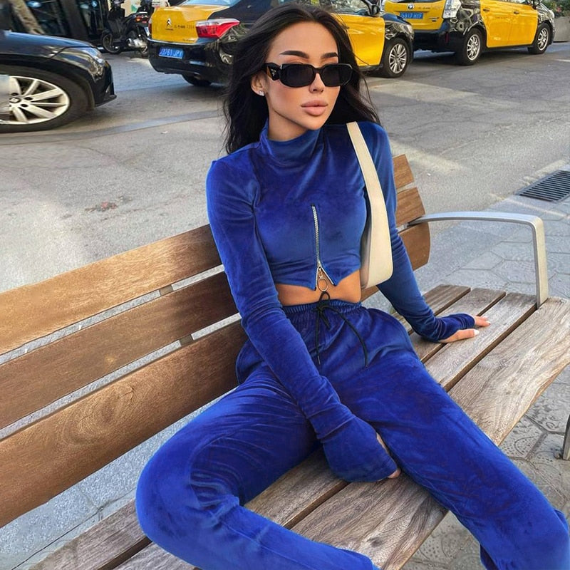 Frau in blauem Samt-Trainingsanzug auf Bank, modisch, urbaner Stil, Sonnenbrille.
