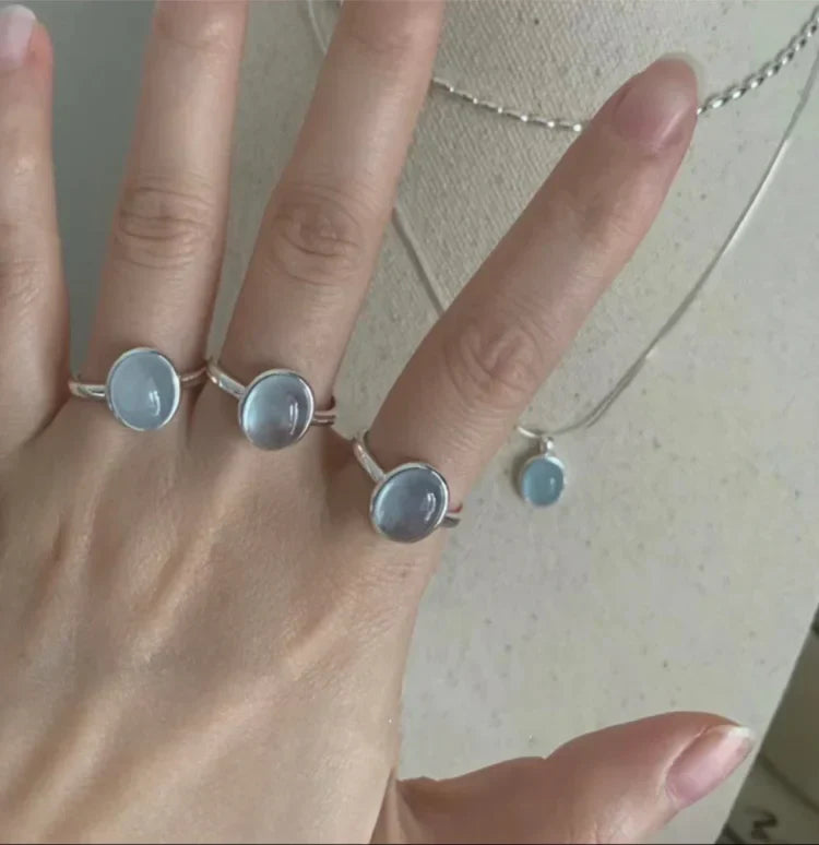 Drei silberne Ringe mit blauen Steinen und passende Halskette auf Hand.