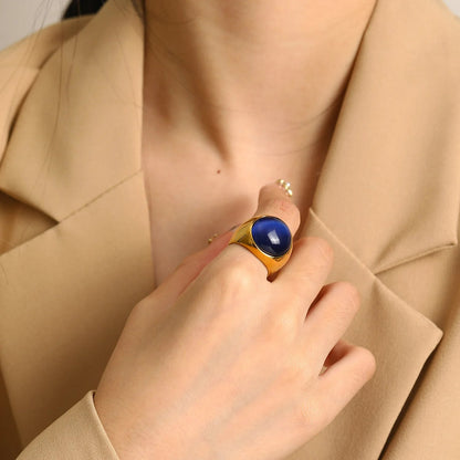Frau trägt goldenen Ring mit blauem Stein, elegantes Schmuckstück, Nahaufnahme, beige Blazer.