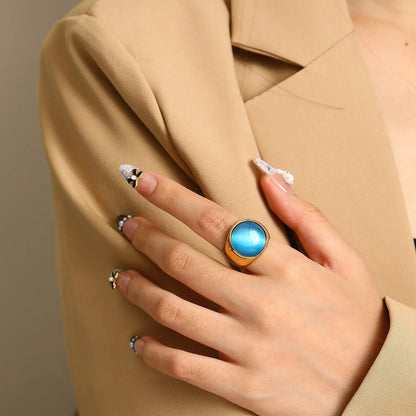 Frau mit blauem Edelsteinring, goldener Fassung, eleganter Look, beige Blazer, stilvolle Maniküre.