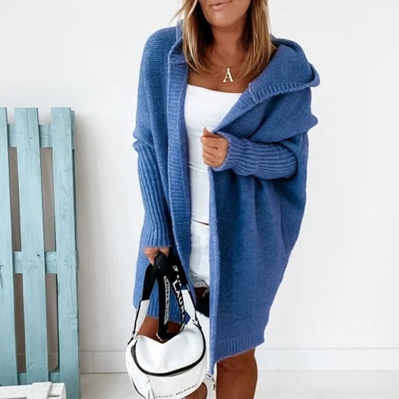 Frau in blauem Strick-Cardigan mit Kapuze, hält weiße Tasche, modisch, gemütlich.