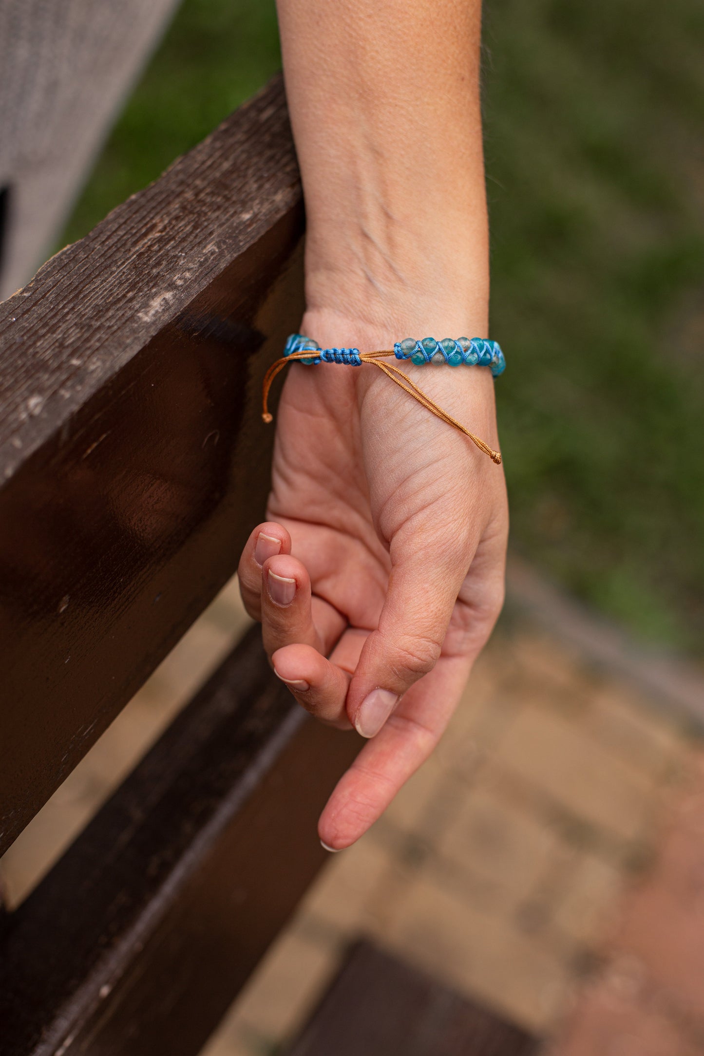 Hand mit blauem Armband aus Perlen auf Holzbank, modisches Accessoire, Damenarmband.