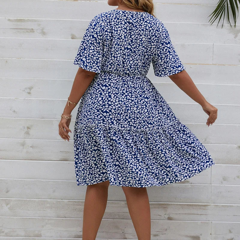 Frau in blau-weißem Sommerkleid mit Blumenmuster vor Holzwand.