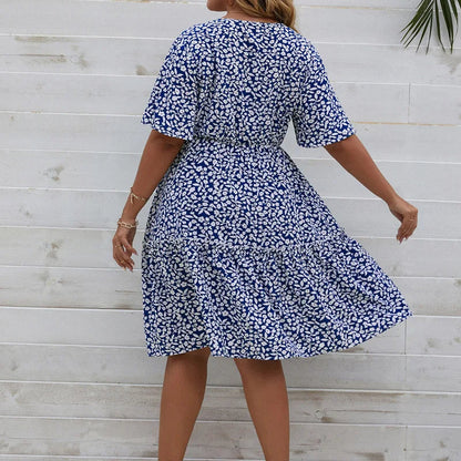 Frau in blau-weißem Sommerkleid mit Blumenmuster vor Holzwand.