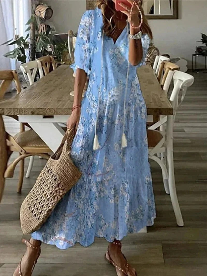 Frau in hellblauem Blumenkleid mit Strohtasche, Sommermode, lässiger Stil, Esszimmer im Hintergrund.