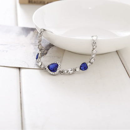 Silbernes Armband mit blauen Herzsteinen und Kristallen auf weißem Hintergrund.