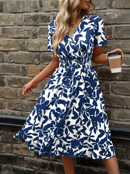 Frau im blau-weiß geblümten Sommerkleid mit Kaffeebecher vor Ziegelwand.