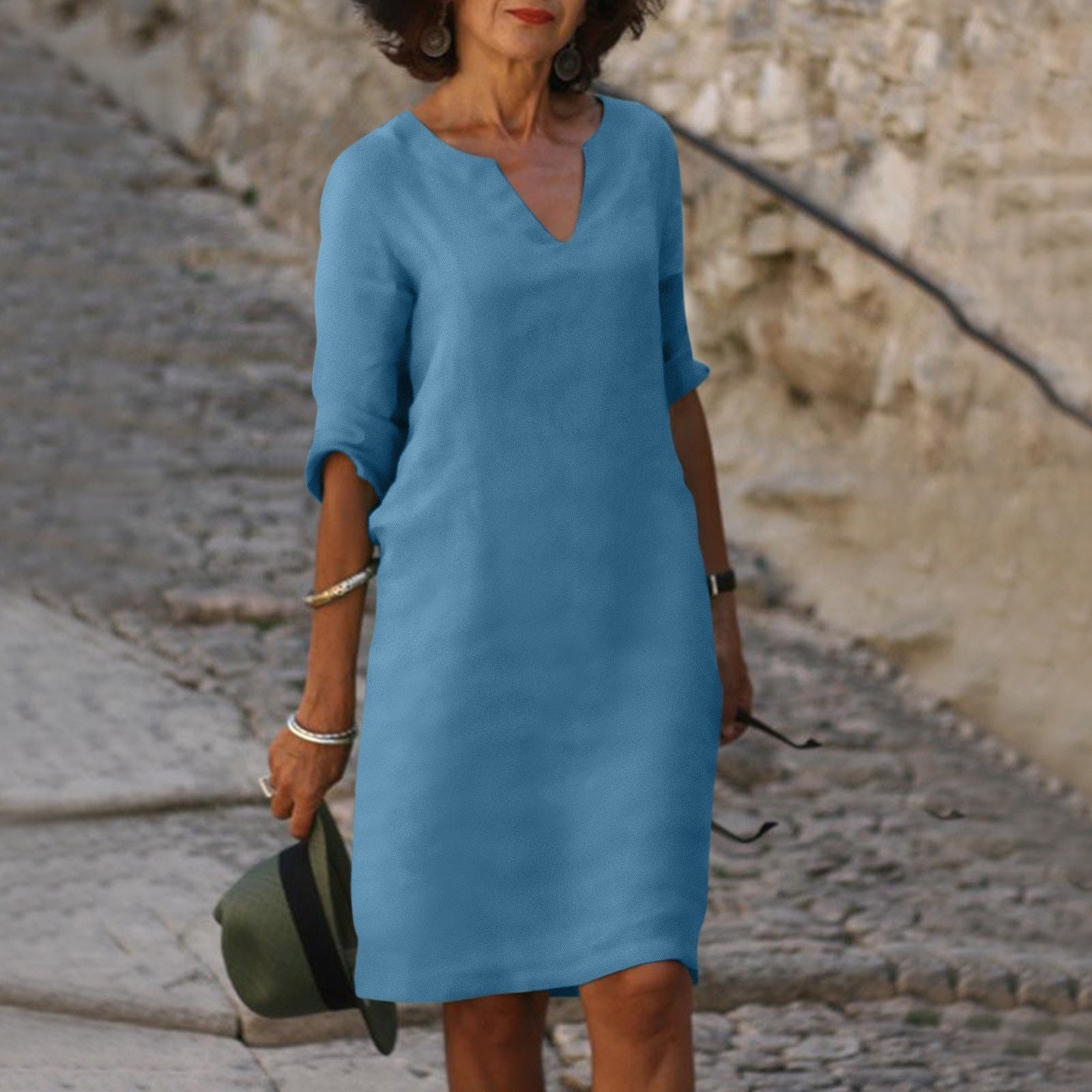 Frau in blauem Leinenkleid, V-Ausschnitt, auf Kopfsteinpflasterweg, Sommermode.