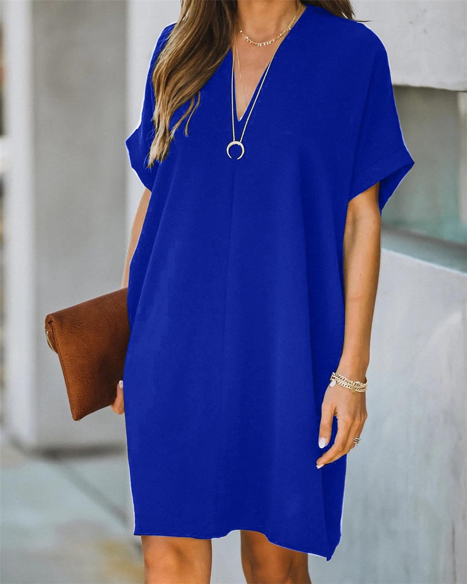 Frau in blauem Sommerkleid mit V-Ausschnitt, braune Clutch, lässiger Stil, modisch.