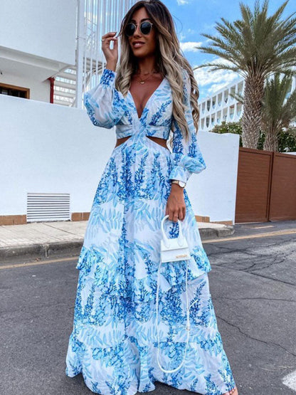 Frau in blau-weißem Maxikleid mit Blumenmuster, Sonnenbrille, kleine weiße Handtasche, draußen.