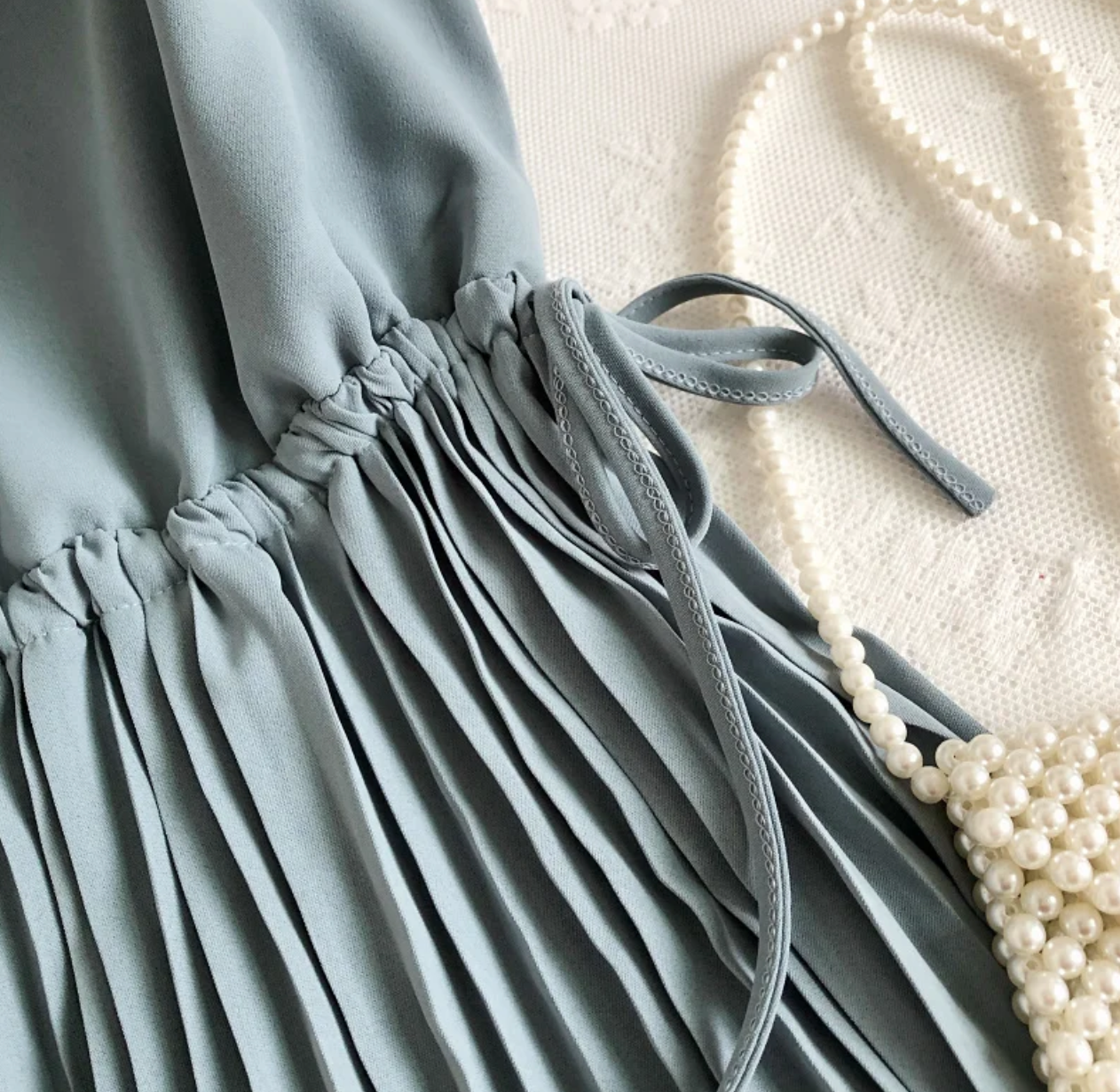 Graues plissiertes Kleid aus Chiffon mit Perlenkette auf Spitze, elegantes Damenoutfit.