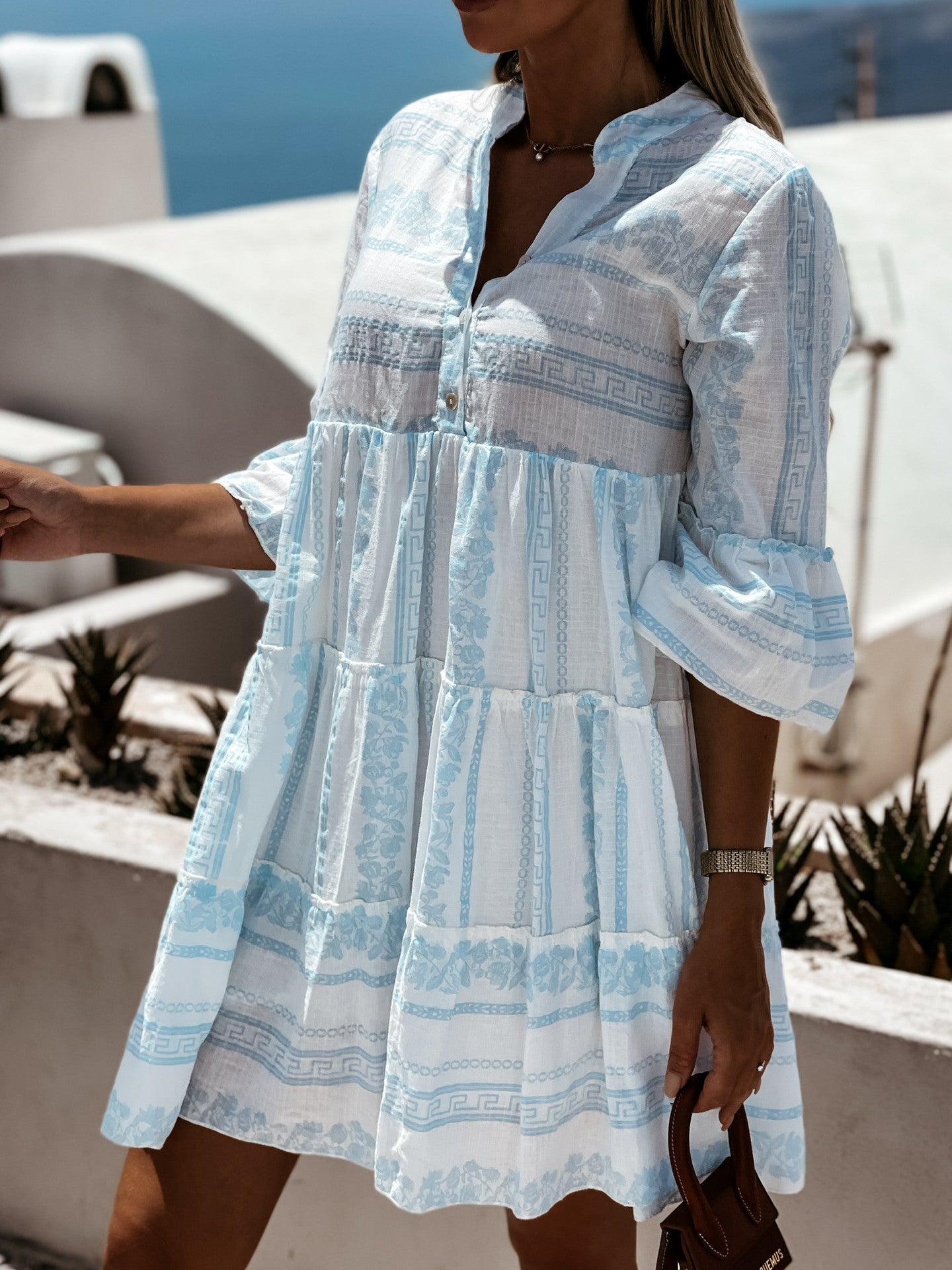 Frau in hellblauem Sommerkleid mit Muster, steht draußen, mediterrane Kulisse.