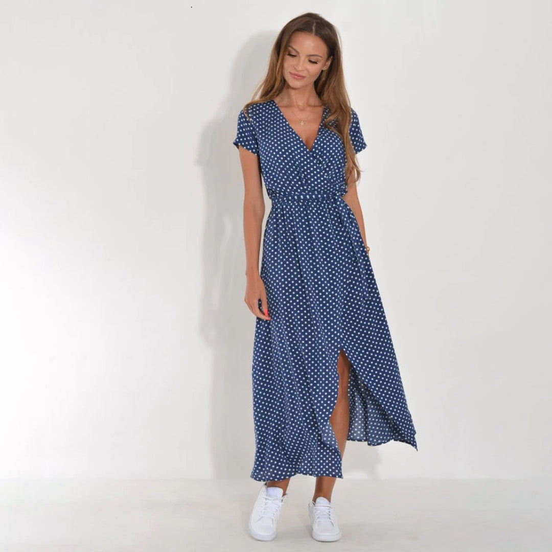 Frau in blauem gepunktetem Maxikleid mit weißen Sneakern vor weißem Hintergrund.