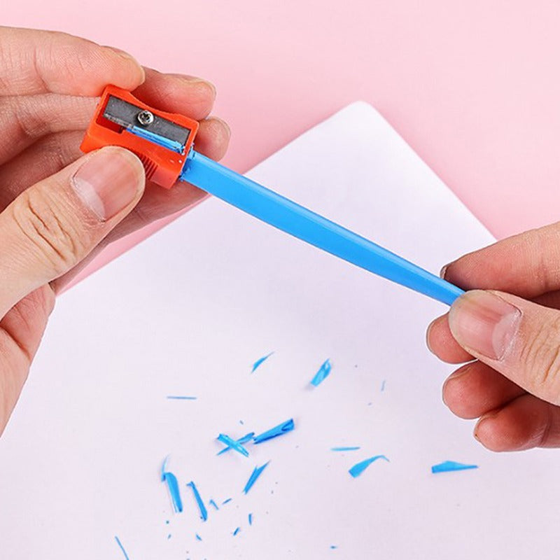 Person hält blauen Bleistiftspitzer, orange, auf rosa Hintergrund mit Papier und Spänen.