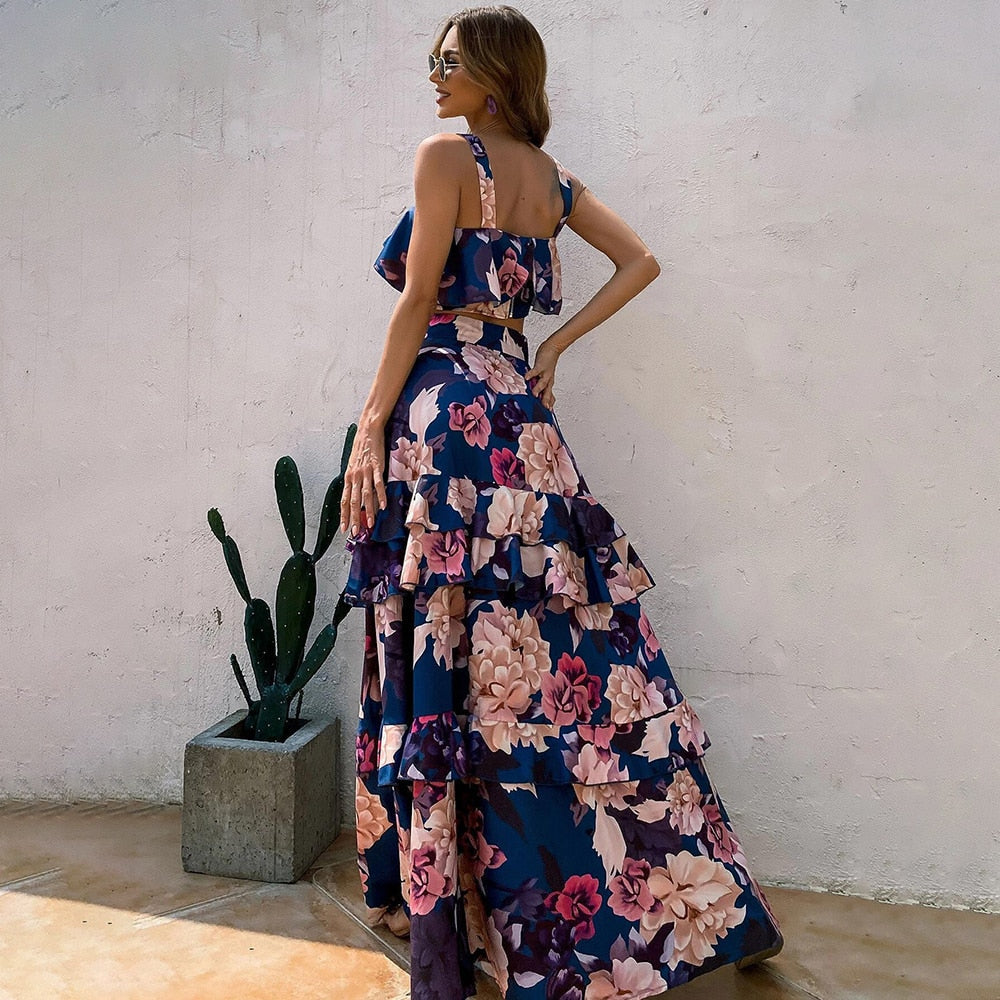 Frau im blauen Blumenkleid mit Rüschen vor weißer Wand und Kaktus in Betonpflanzer.