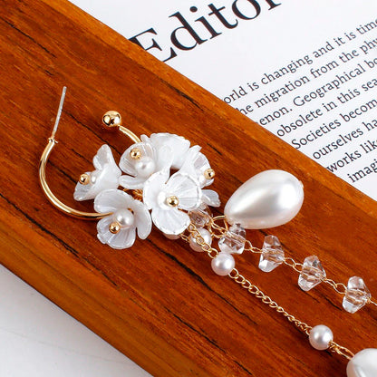 Goldene Ohrringe mit weißen Blumen, Perlen und Kristallen auf Holzuntergrund.