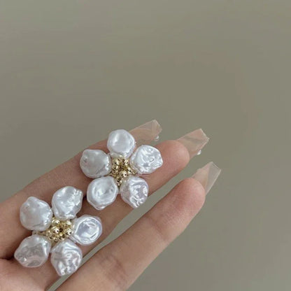 Weiße Perlenblumen-Ohrringe mit goldenen Details auf Hand, eleganter Schmuck, modisch.