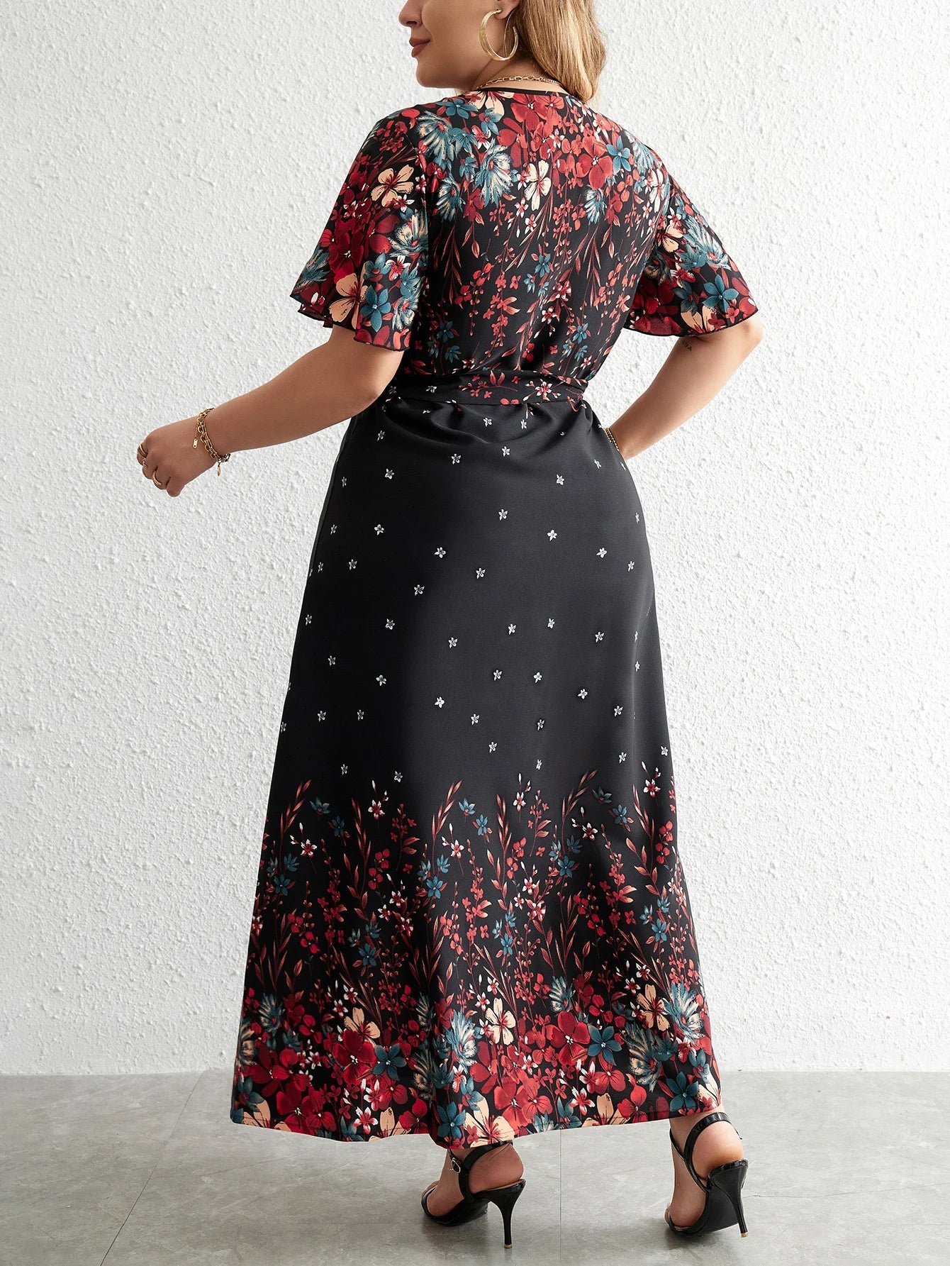 Frau in langem, schwarzem Blumenkleid mit kurzen Ärmeln und roten Blumenmuster, Rückansicht.