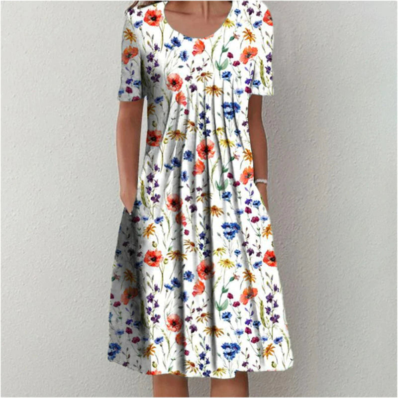 Frau in weißem, geblümtem Sommerkleid mit kurzen Ärmeln vor neutralem Hintergrund.