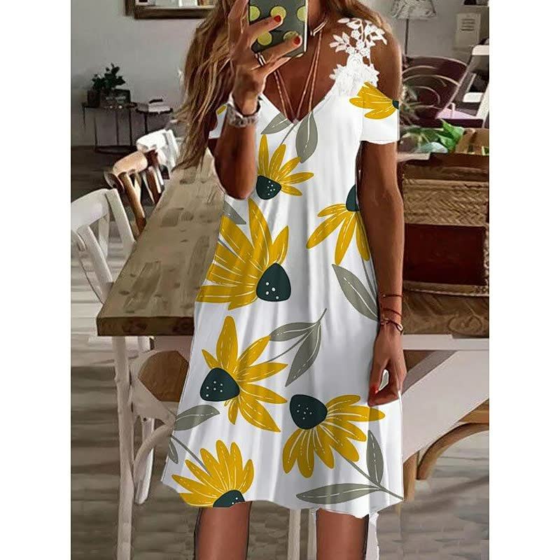 Frau in weißem Sommerkleid mit gelbem Blumenmuster, schulterfrei, im Wohnzimmer.